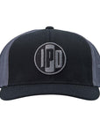 A structured trucker hat with dark grey mesh on the back and a cotton twill black front. In the middle of the front is an embroidered IPD black and dark grey patch logo. This hat has a curved brim and adjustable snap back.