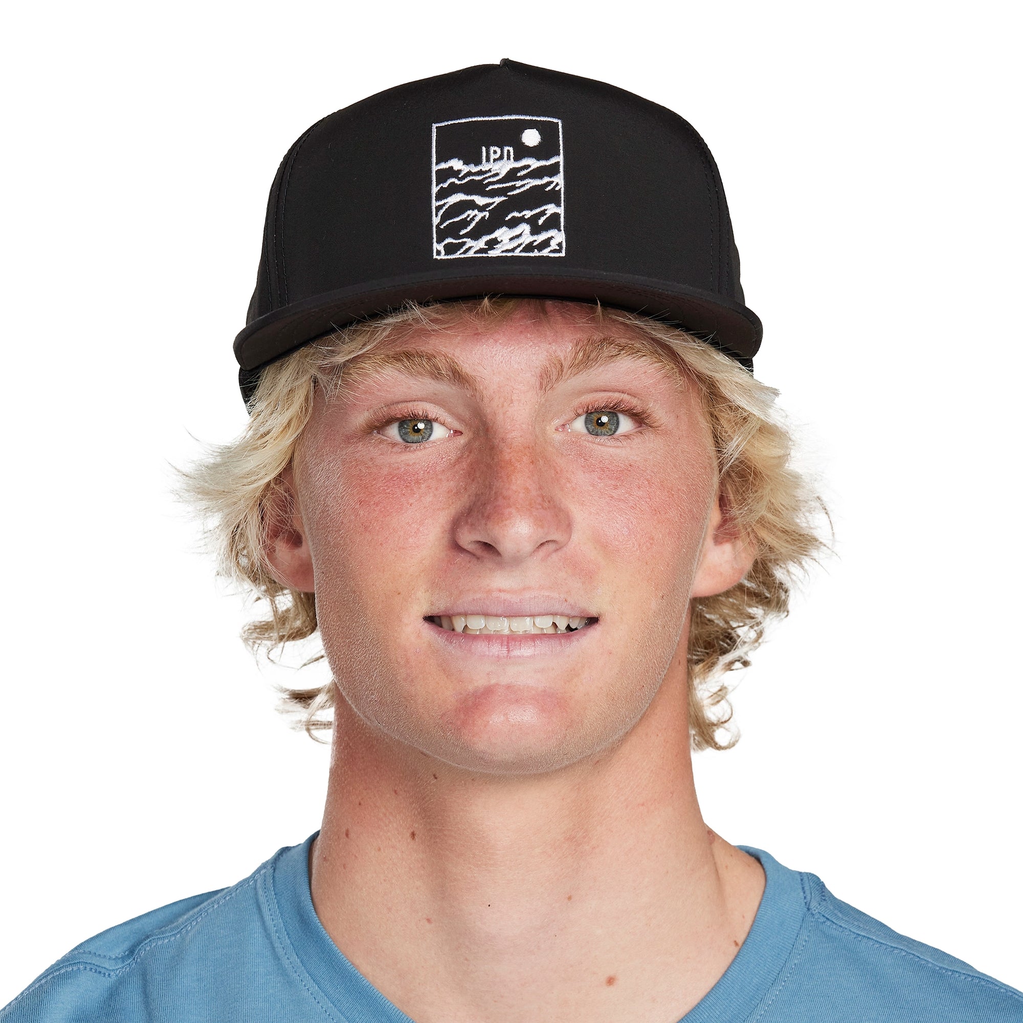 Headshot of a young man wearing a black hat with a white, rectangular framed print of choppy water with the letters I P D above the water and a circular sun in the top right corner of the frame.
