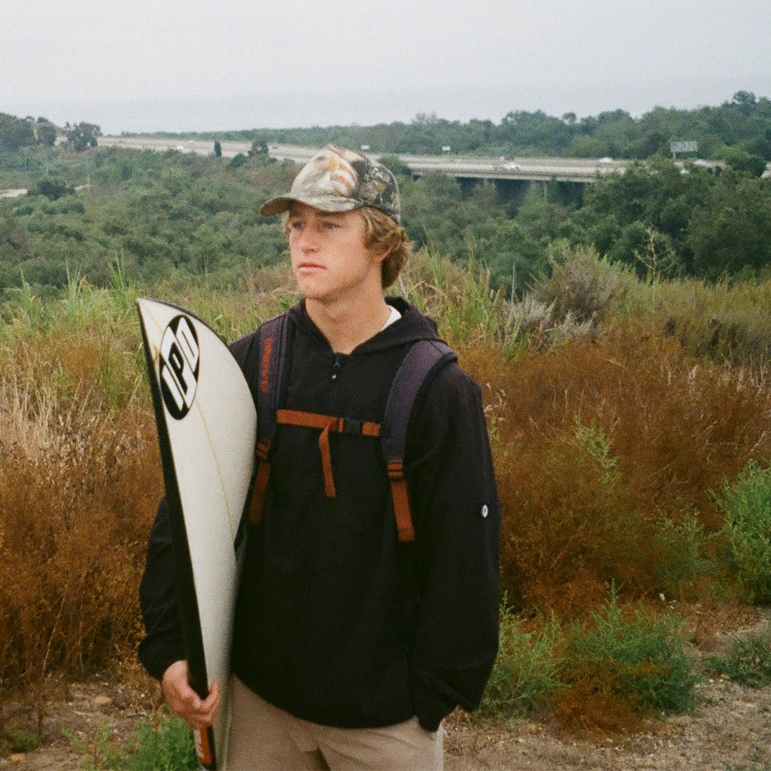 Surfer holding his surfboard while wearing a black water repellent hooded jacket.