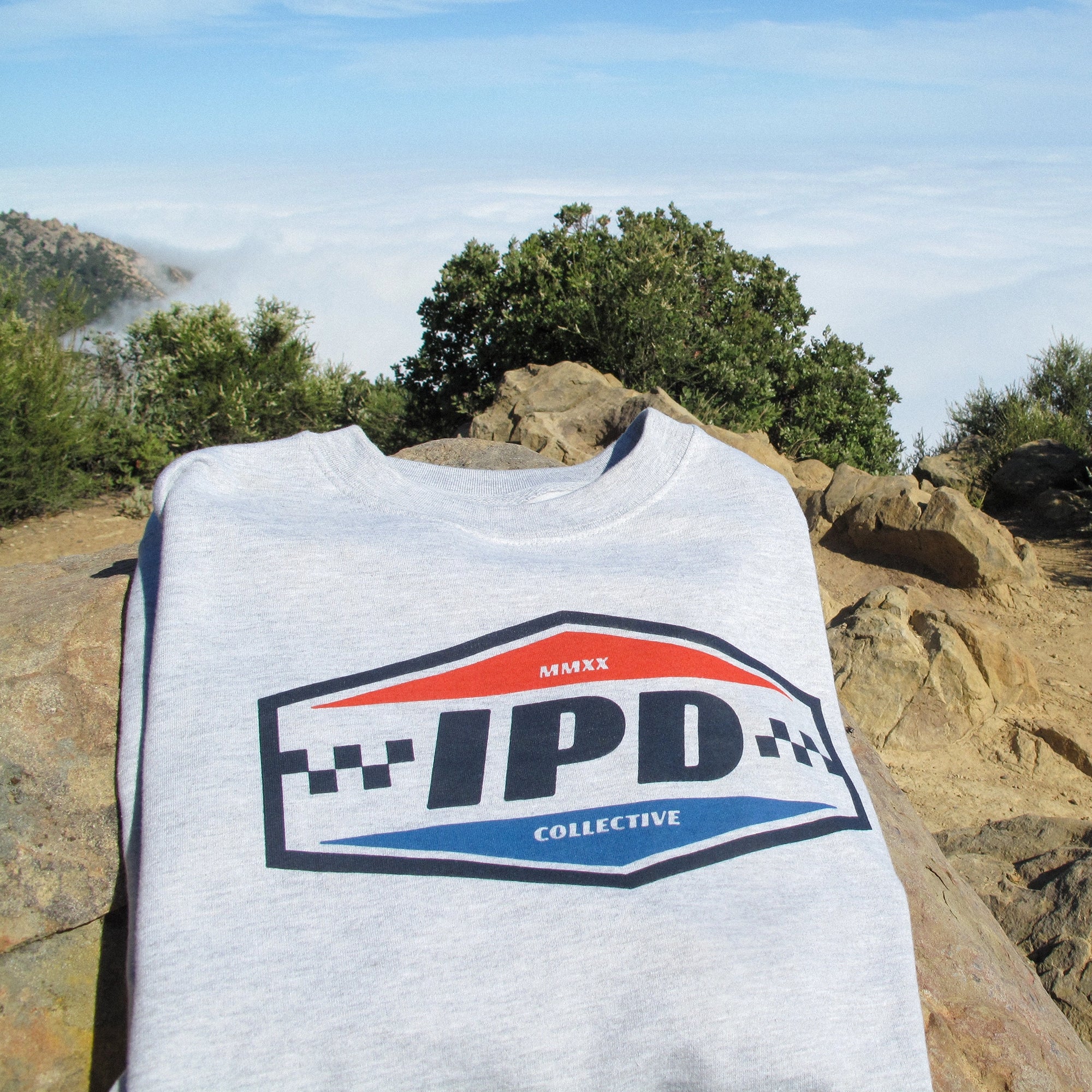IPD logo sweatshirt displayed on rocks with a scenic background.