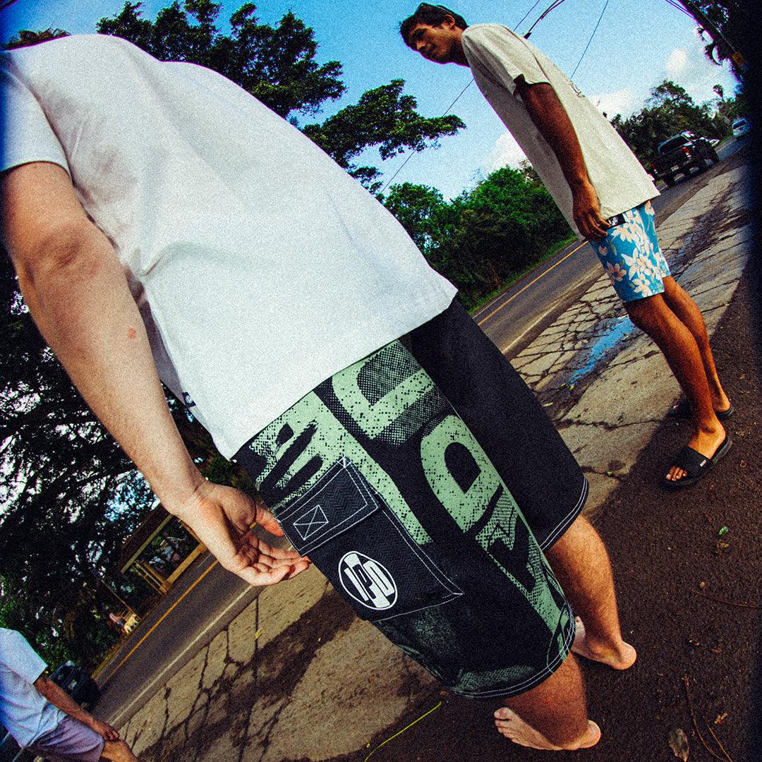 man wearing mens faceplant y2k fit 22" boardshort in black standing with friends looking at beach taken in fisheye lense