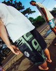 man wearing mens faceplant y2k fit 22" boardshort in black standing with friends looking at beach taken in fisheye lense