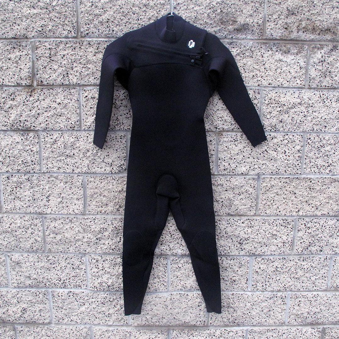 men's black full body wetsuit hanging on wall. I P D circle logo on left shoulder along with chest zipper that runs across to right side. 