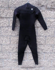men's black full body wetsuit hanging on wall. I P D circle logo on left shoulder along with chest zipper that runs across to right side. 