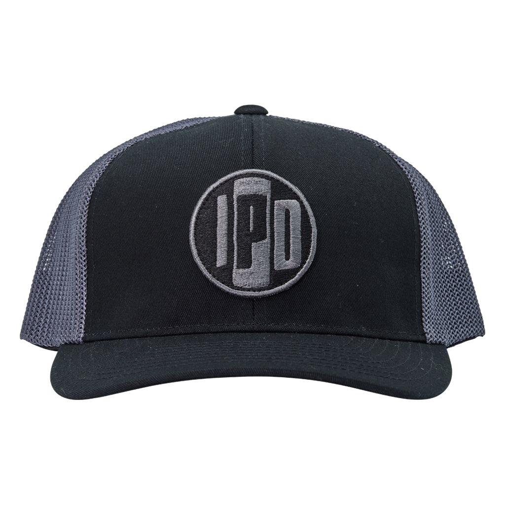 A structured trucker hat with dark grey mesh on the back and a cotton twill black front. In the middle of the front is an embroidered IPD black and dark grey patch logo. This hat has a curved brim and adjustable snap back.